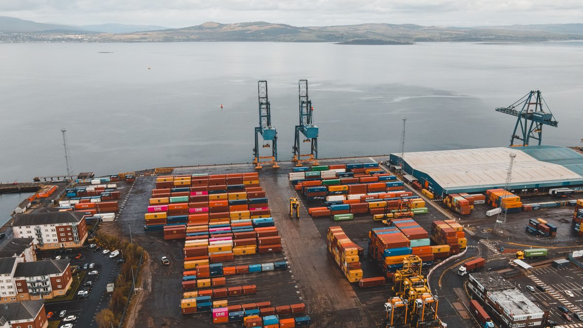 Aerial shot of a busy container port in Scotland with cranes and colorful cargo containers.