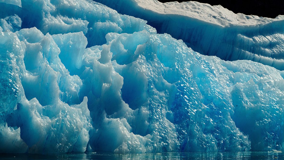 A stunning view of a blue iceberg with intricate textures, floating in the calm ocean.