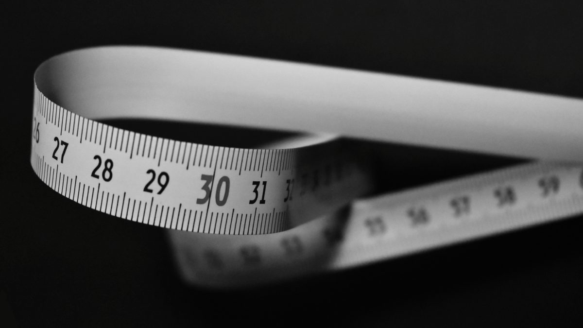 Black and white image of a flexible measuring tape curling on a dark background.