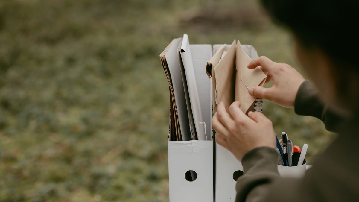 Person sorting documents in folders outdoors, hands visible, neutral tone.