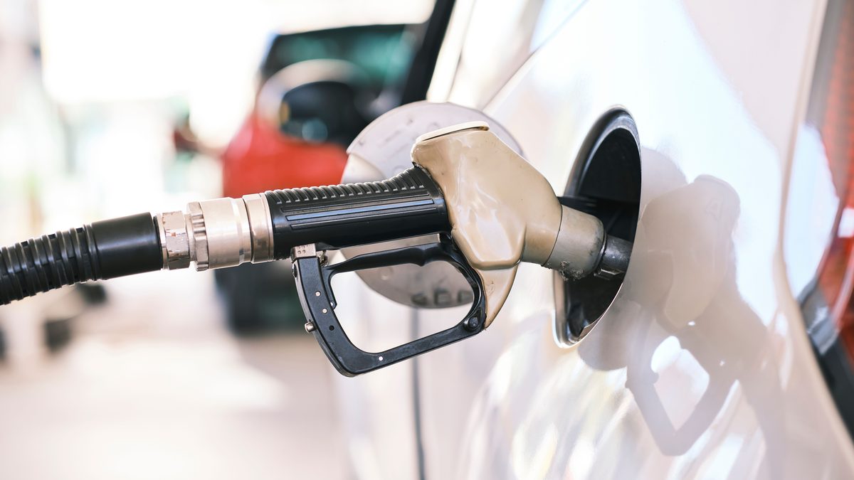 Fuel nozzle inserted in car at a gas station, close-up view emphasizing energy and transportation themes.