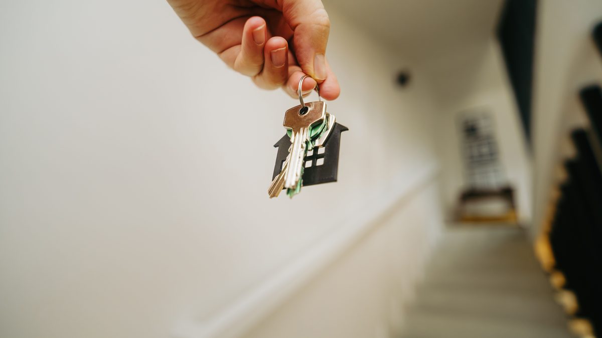 Close-up of a hand holding a keychain in the shape of a house, symbolizing real estate and property ownership.