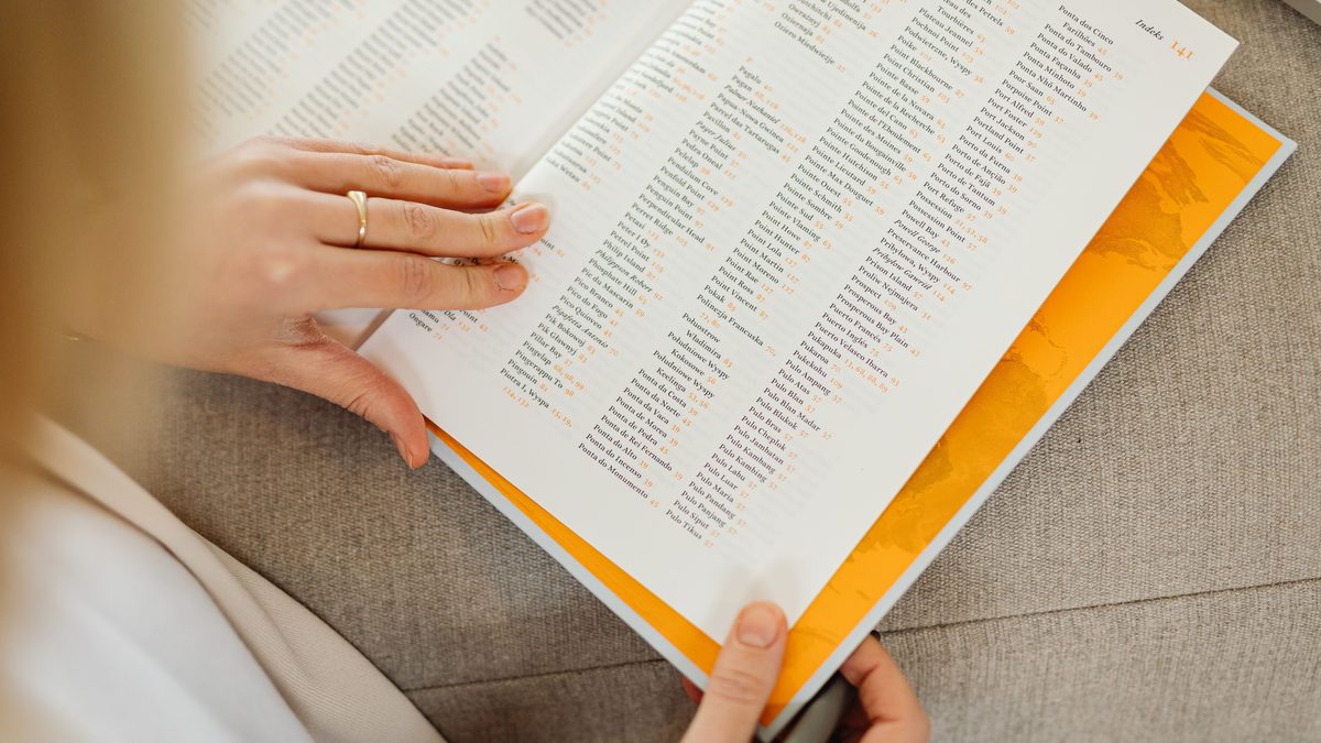 Close-up of a woman's hands holding an open book on a sofa, focusing on text details.