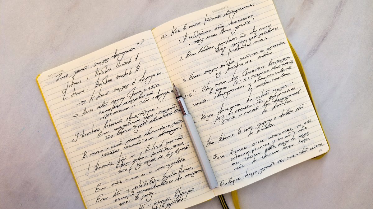 Open notebook with cursive handwritten notes on marble surface and a pen resting on pages.