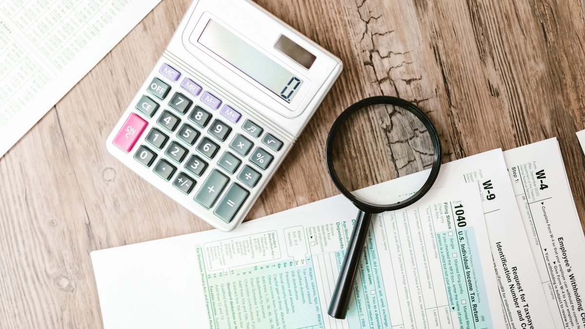 Tax forms laid out with a calculator and magnifying glass on a wooden surface, perfect for finance themes.