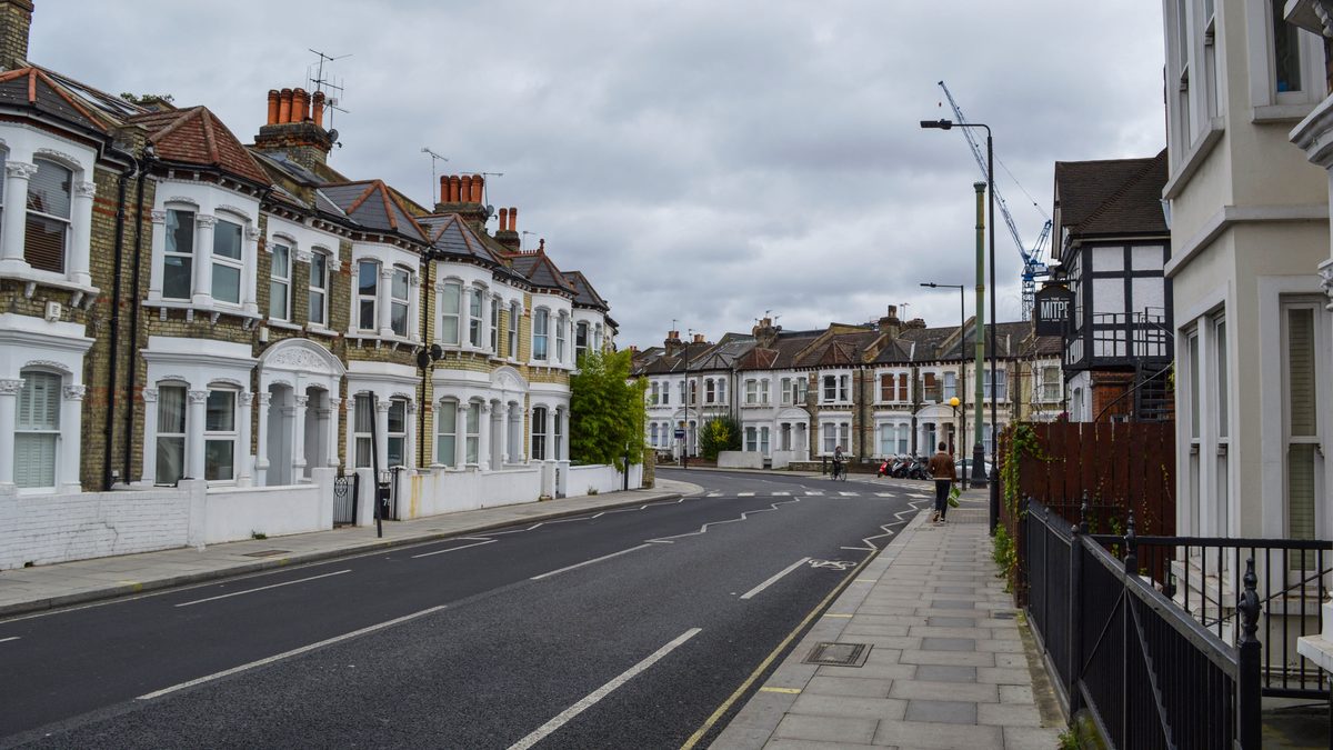 Row of modern low-rise houses along a concrete street with a kerbed pavement, photographed under a heavy grey overcast sky.