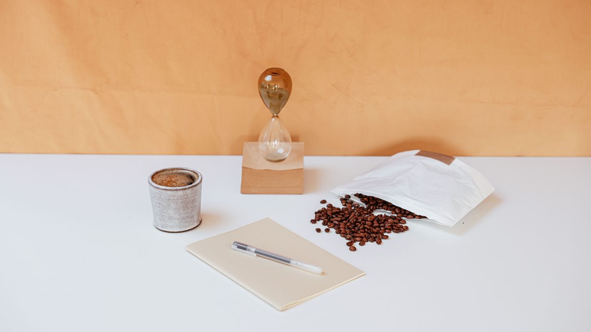 A minimalist workspace featuring coffee beans, an hourglass, a notebook, and a pen for creative inspiration.