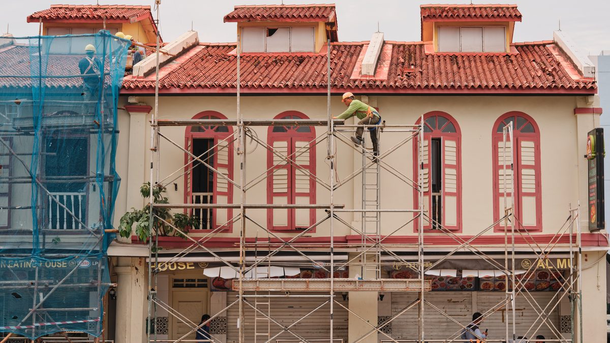Workers on scaffolding renovating a historic building facade with red roof and tall windows.