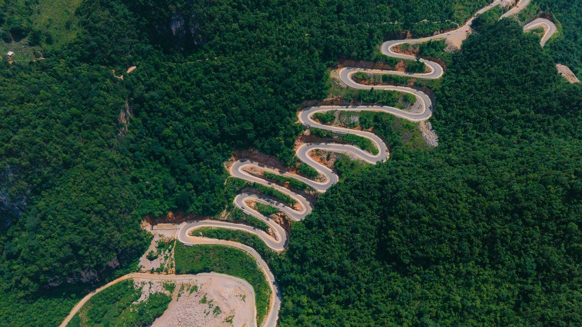 Scenic aerial shot of a winding mountain road through lush green forests, showcasing nature's beauty.